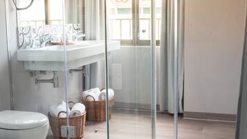A bathroom with a glass shower enclosure, a white sink, and two wicker baskets with towels.
