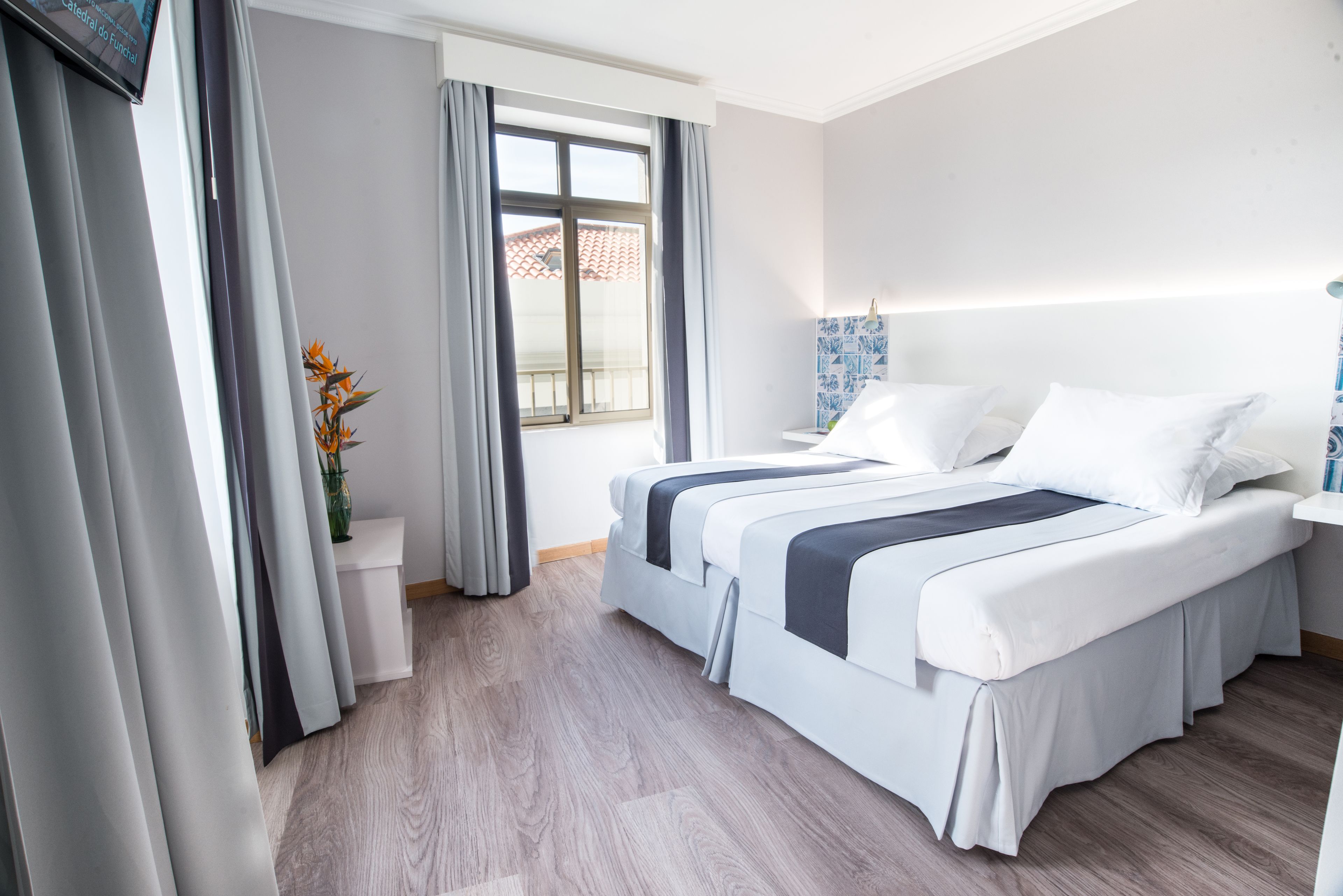A hotel room with a large bed, a bedside table, a window with curtains, and a view of the outside.