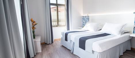 A hotel room with a large bed, a bedside table, a window with curtains, and a view of the outside.