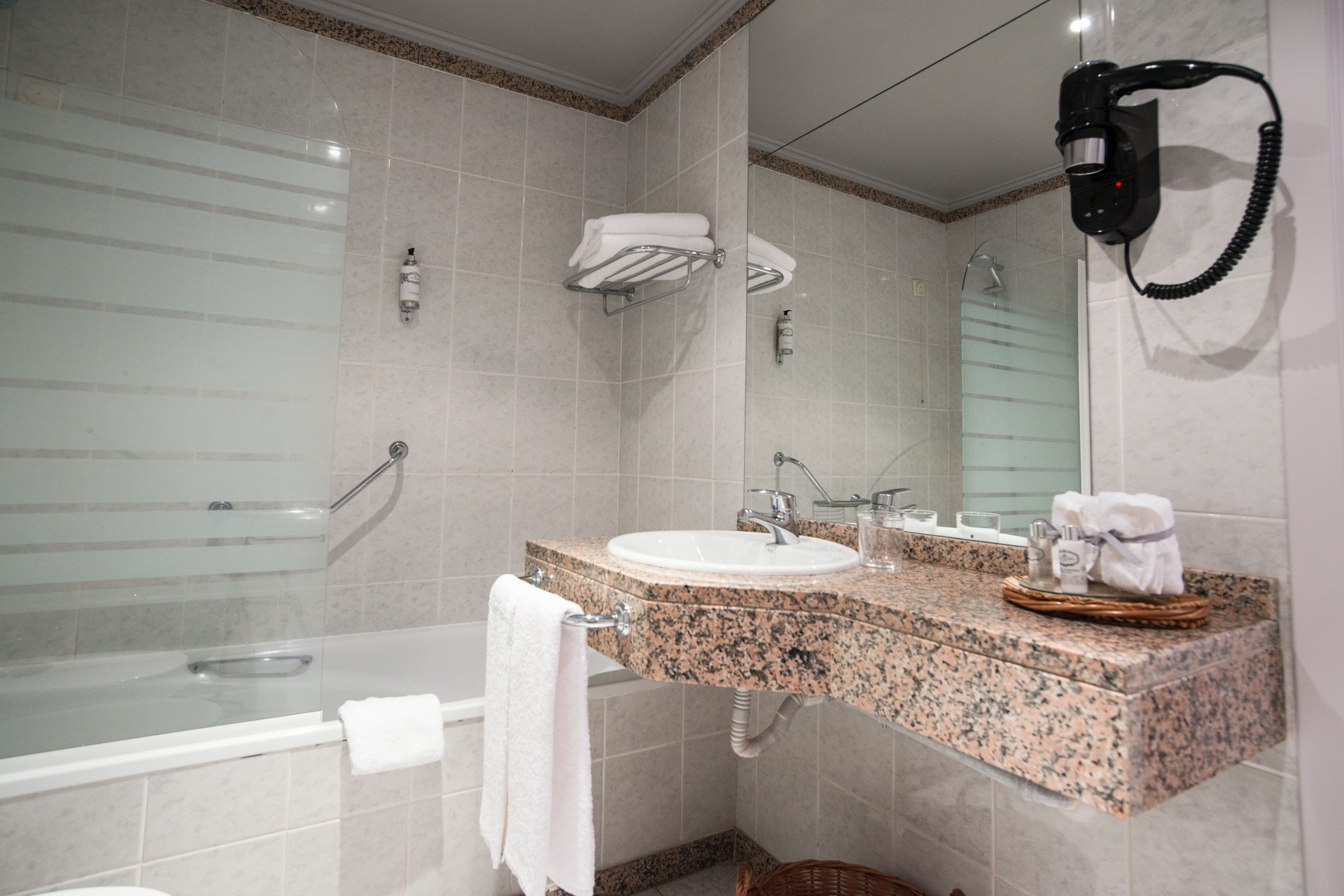 A bathroom with a bathtub, a sink, a mirror, and a hairdryer mounted on the wall.