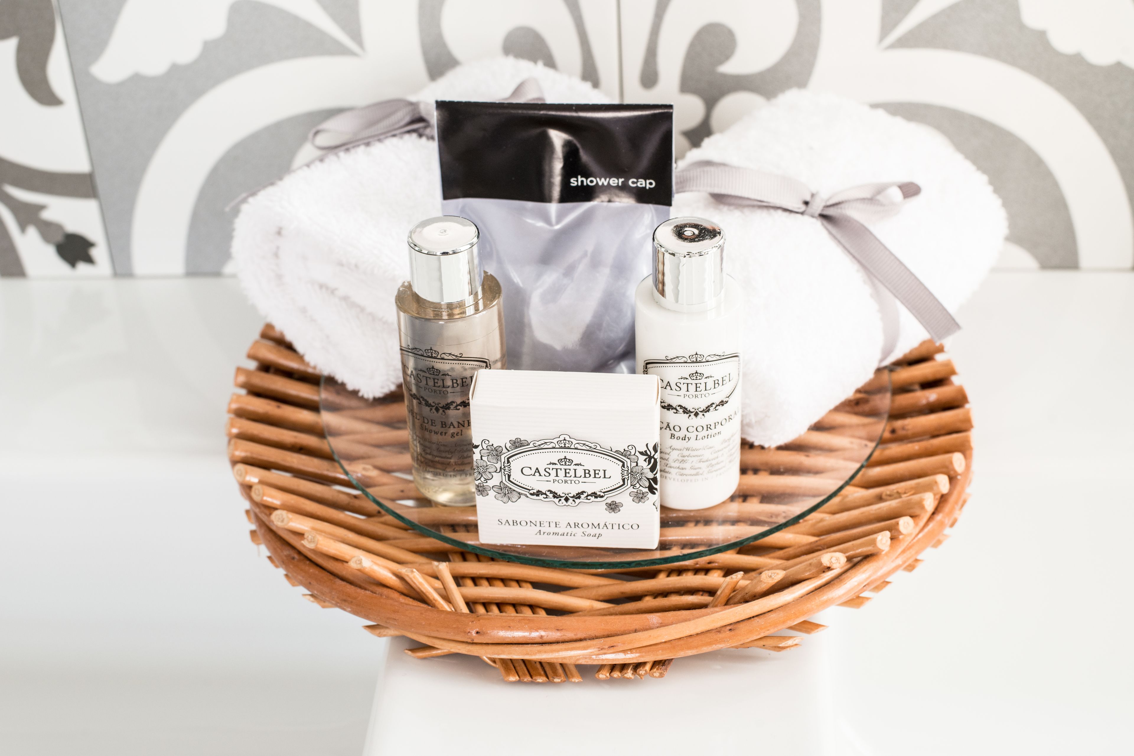 Un panier en osier contenant un bonnet de douche, deux flacons de lotion pour le corps de la marque Castelbel et un savon.