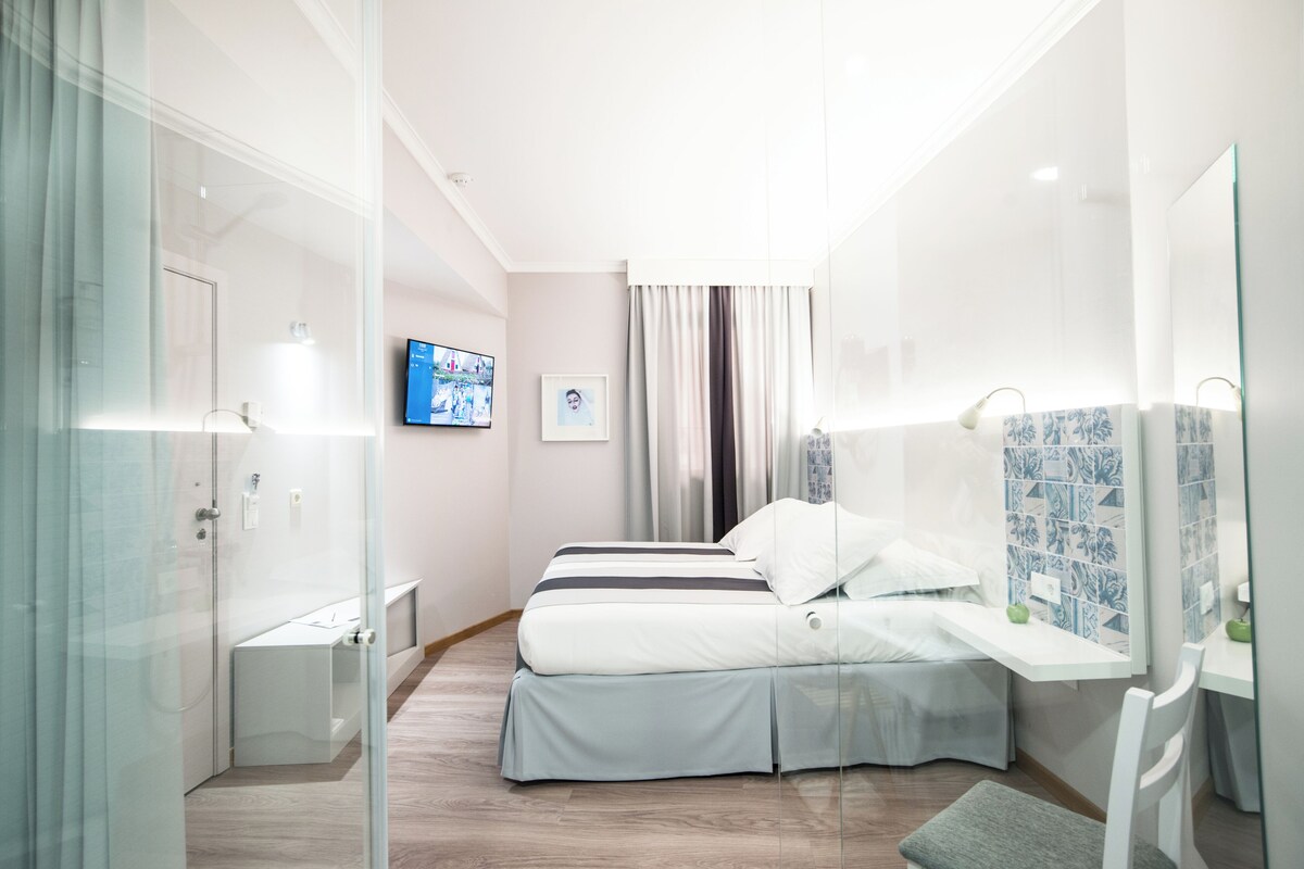 A modern hotel room with a bed, bedside tables, a TV, and a bathroom with a shower and toilet.