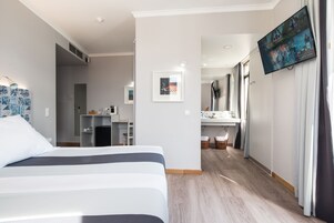 Una camera d'albergo con un letto, una scrivania, uno specchio e una TV a parete.