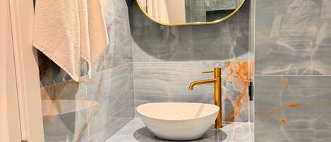 A modern bathroom with a marble vanity, a gold faucet, and a large mirror.