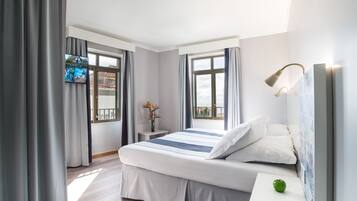 Una habitación de hotel moderna con una cama grande, una mesita de noche pequeña, un televisor montado en la pared y una ventana con cortinas.