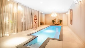 A swimming pool with a tiled floor, a chair, a mirror, and a chandelier. - Sé Boutique Hotel (Funchal)
