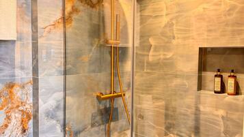 Een moderne douche met een glazen cabine, marmeren wanden en een handdouche.