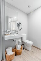 Un bagno moderno con un lavandino bianco, un water e una doccia. Sono presenti due cesti di vimini con asciugamani.