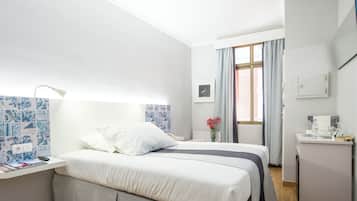 A hotel room with a bed, a desk with a lamp, a small table with a coffee maker, and a window with curtains.