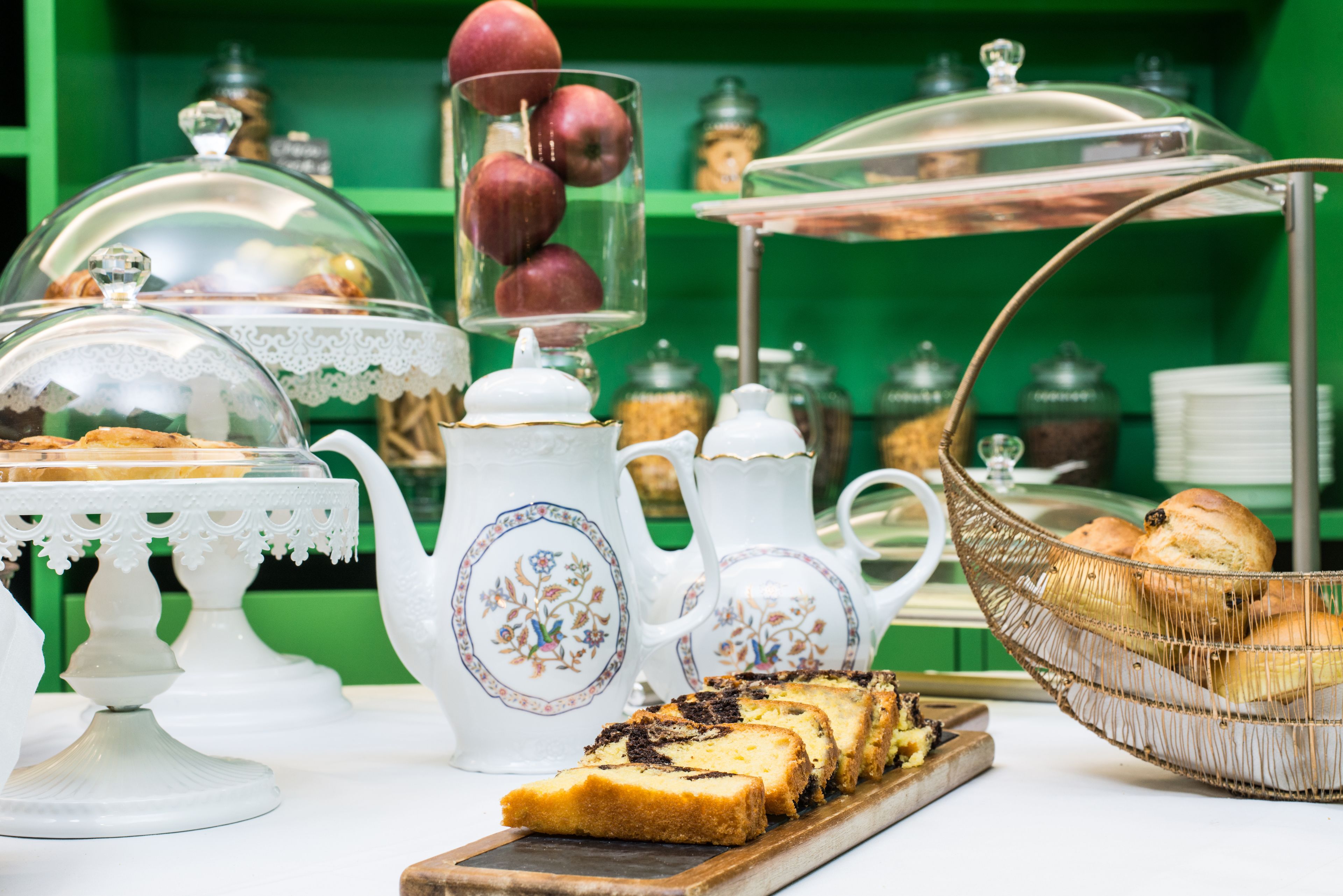 A breakfast buffet with various pastries, a teapot, and a fruit display.