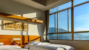 Quarto de hotel com duas camas, uma cabeceira de madeira, uma janela ampla com vista para as montanhas e uma obra de arte emoldurada na parede.