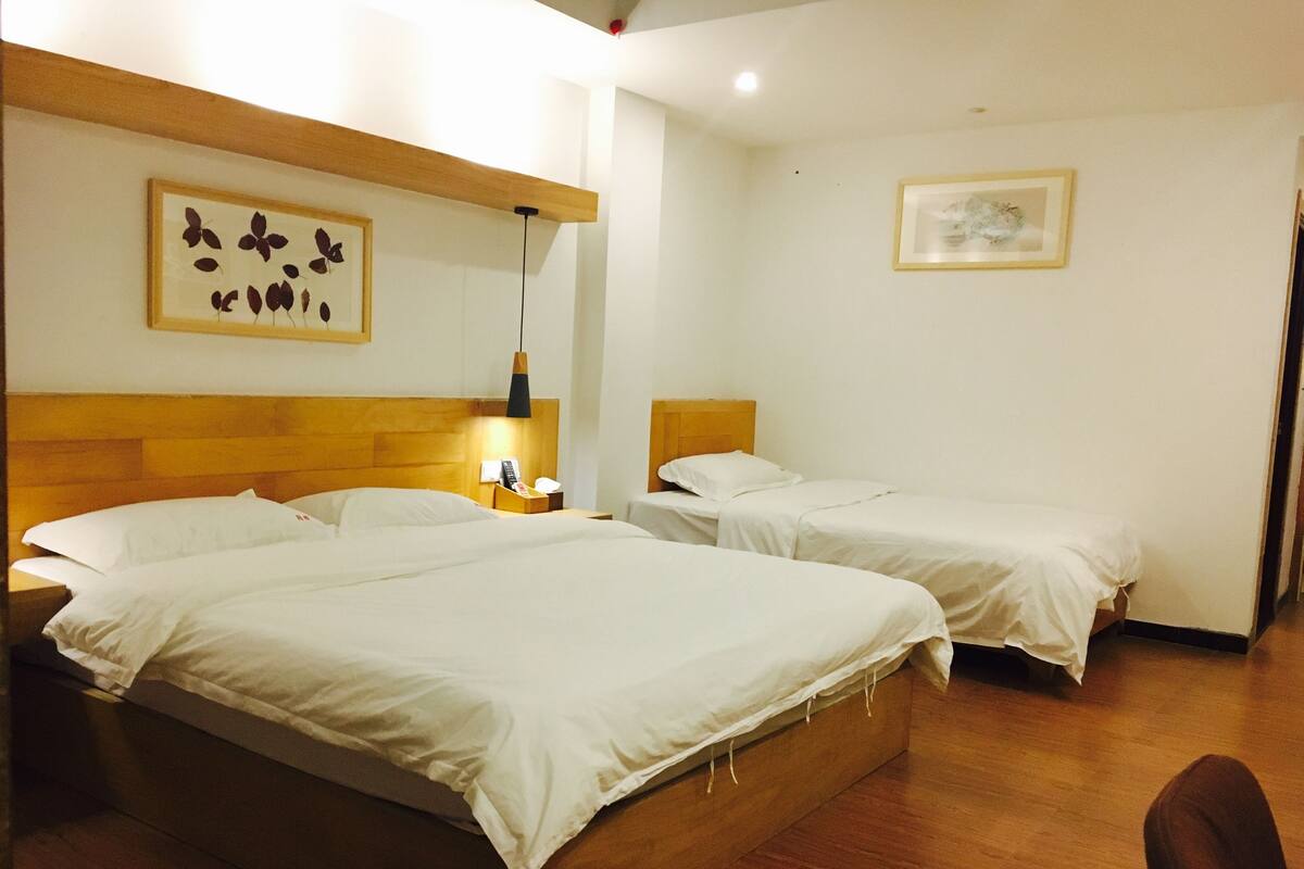 A hotel room with two beds, wooden headboards, a nightstand with a lamp, and a framed picture on the wall.