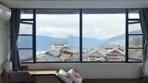 Quarto com uma grande janela com vista para edifícios tradicionais e montanhas.