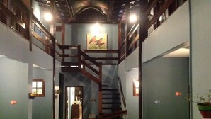 Un pasillo estrecho con una escalera de madera que sube a un nivel superior. Hay dos puertas a cada lado del pasillo y una pequeña ventana en la pared izquierda.