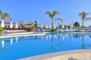 A pool area with lounge chairs and umbrellas, surrounded by palm trees. - Lebay Beach Hotel (Oroklini)