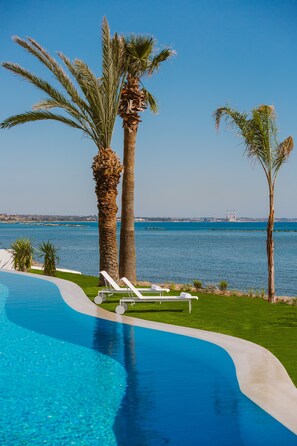 A pool with a curved edge, palm trees, and a view of the sea. - Lebay Beach Hotel (Oroklini)