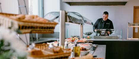 A buffet setup with various food items and a chef preparing food.