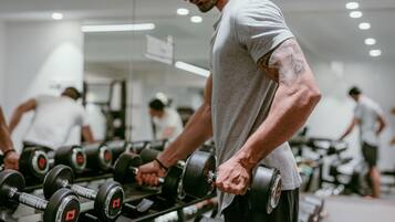 Un gimnasio con filas de mancuernas y personas ejercitándose.