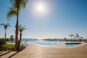 Terraza de madera que da a una piscina, con palmeras y vista al océano.