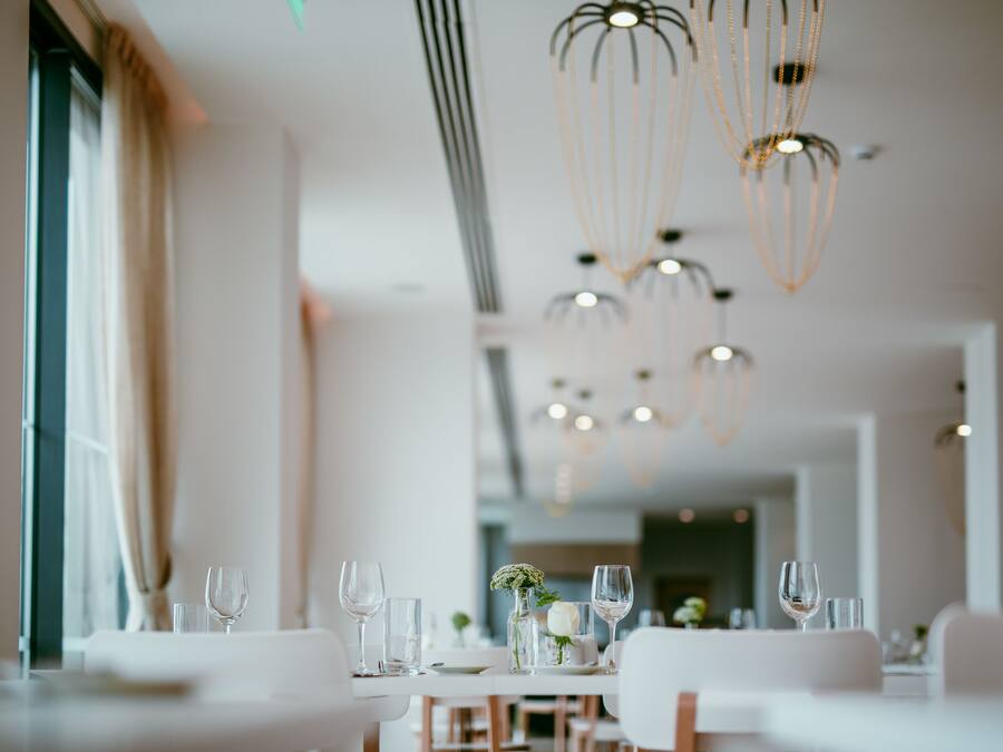 Un espace repas avec des tables dressées pour le service, agrémenté de luminaires suspendus et offrant une vue sur l’intérieur.