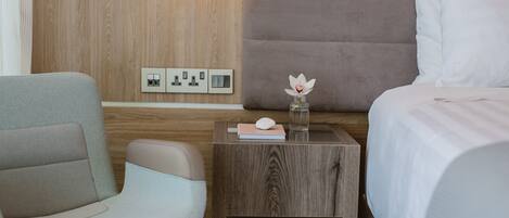 A hotel room with a wooden headboard, a bedside table with a vase of flowers, a chair, and a bed with white bedding.