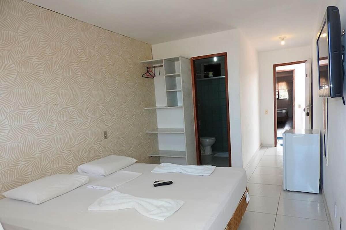 Une chambre d’hôtel avec un lit, une armoire, une télévision et une salle de bain visible à travers une porte ouverte.