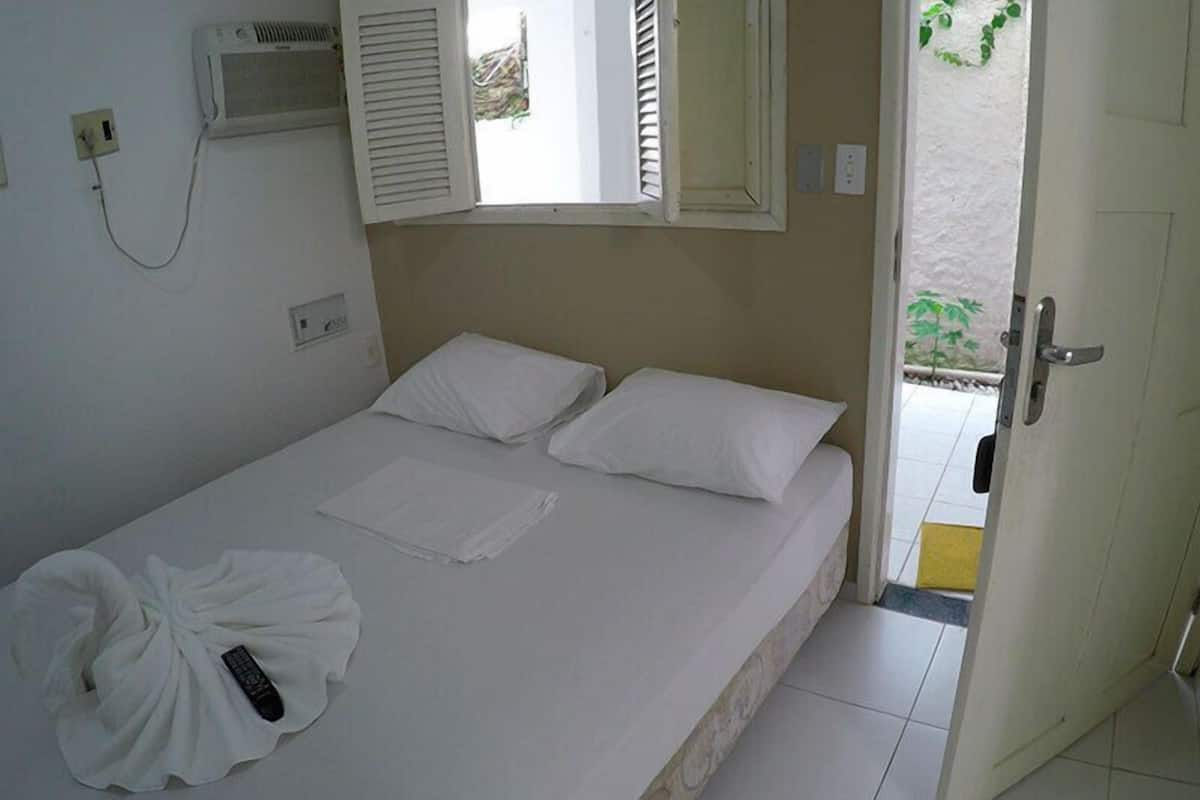 Un lit simple avec du linge de lit blanc, une télécommande et un climatiseur fixé au mur.