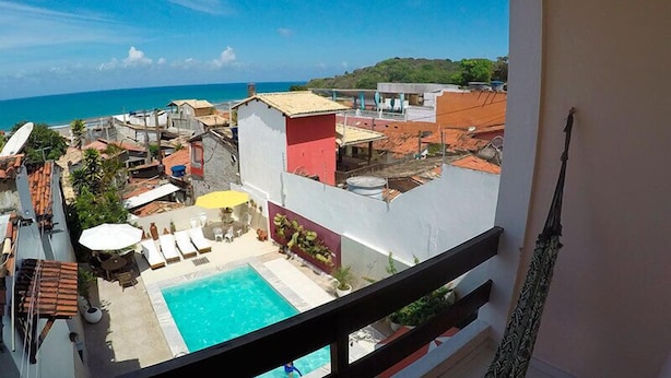 A balcony with a view of a swimming pool, a beach, and surrounding buildings. - Pousada Praiana (Tibau do Sul)