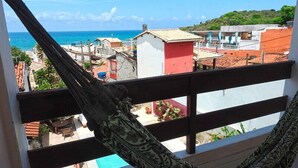 A hammock on a balcony overlooking a coastal town with buildings and a clear blue sky. - Pousada Praiana (Tibau do Sul)