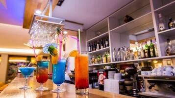 Zona de bar con cócteles coloridos y una estantería llena de botellas de licores al fondo.