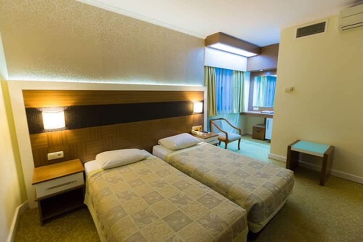 A hotel room with two beds, a nightstand, a chair, a desk, and a mirror.