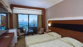 Habitación de hotel con balcón, escritorio, dos camas y vista al océano.
