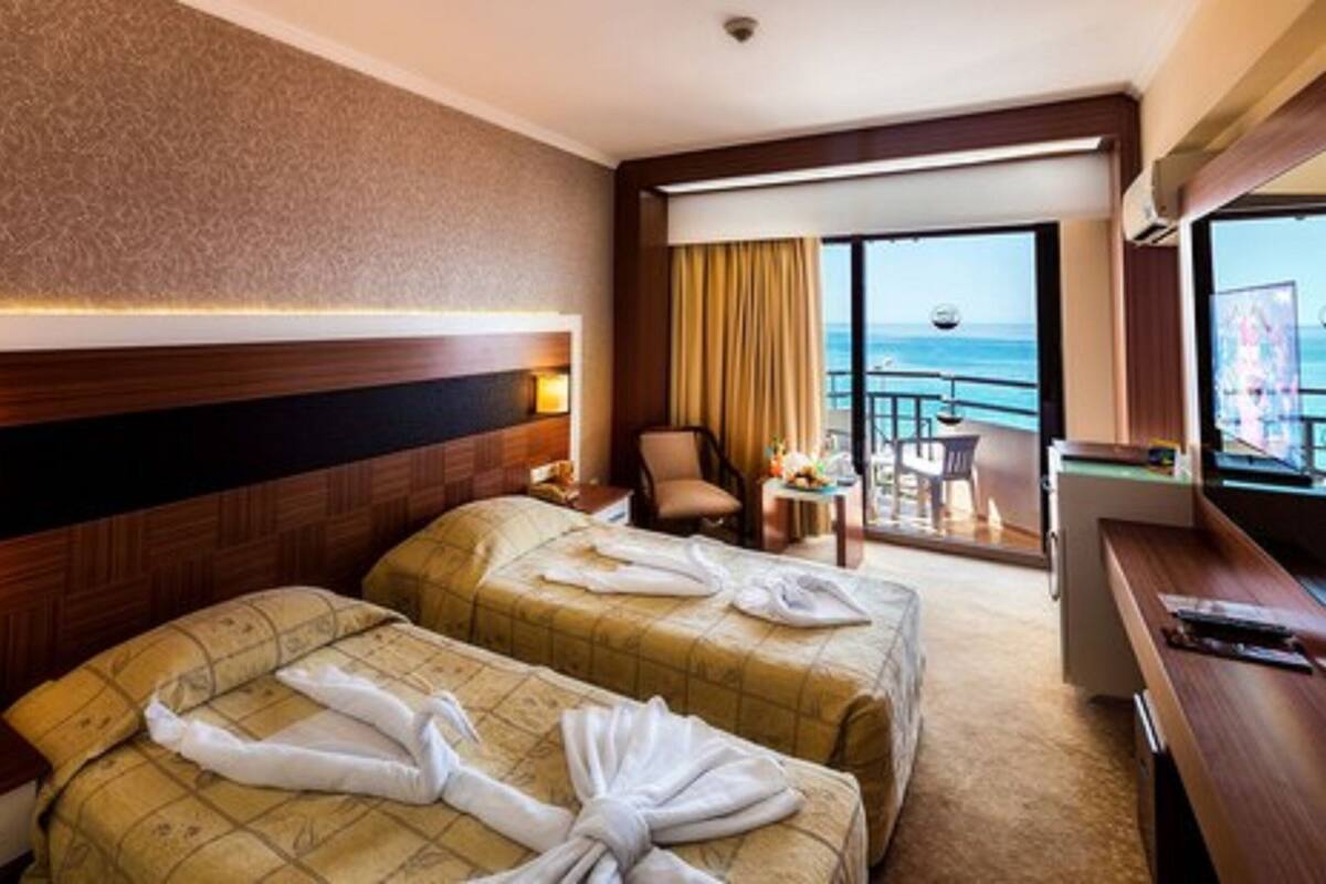 A hotel room with two beds, a balcony with a view of the sea, a desk, and a chair.
