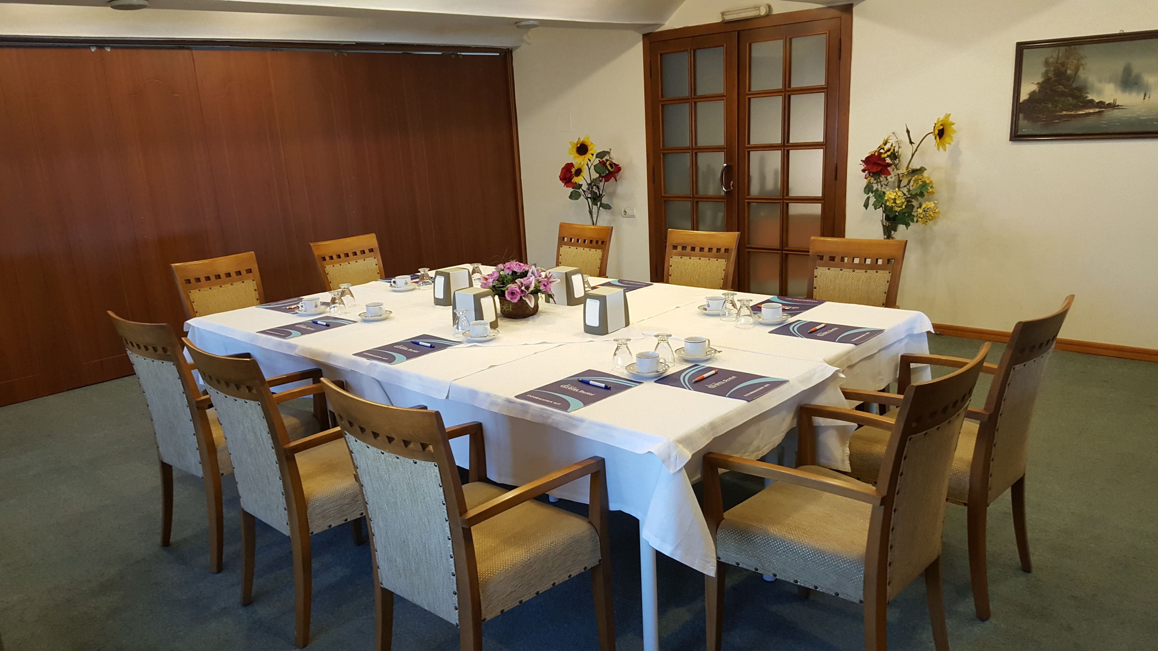 Un salón de conferencias con una gran mesa, sillas, tarjetas de identificación y centros de mesa florales.