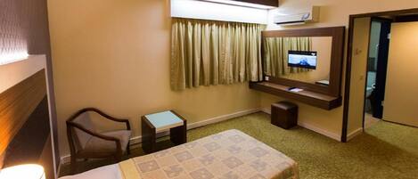 Habitación de hotel con cama, una silla, una mesita, televisión montada en la pared y aire acondicionado.