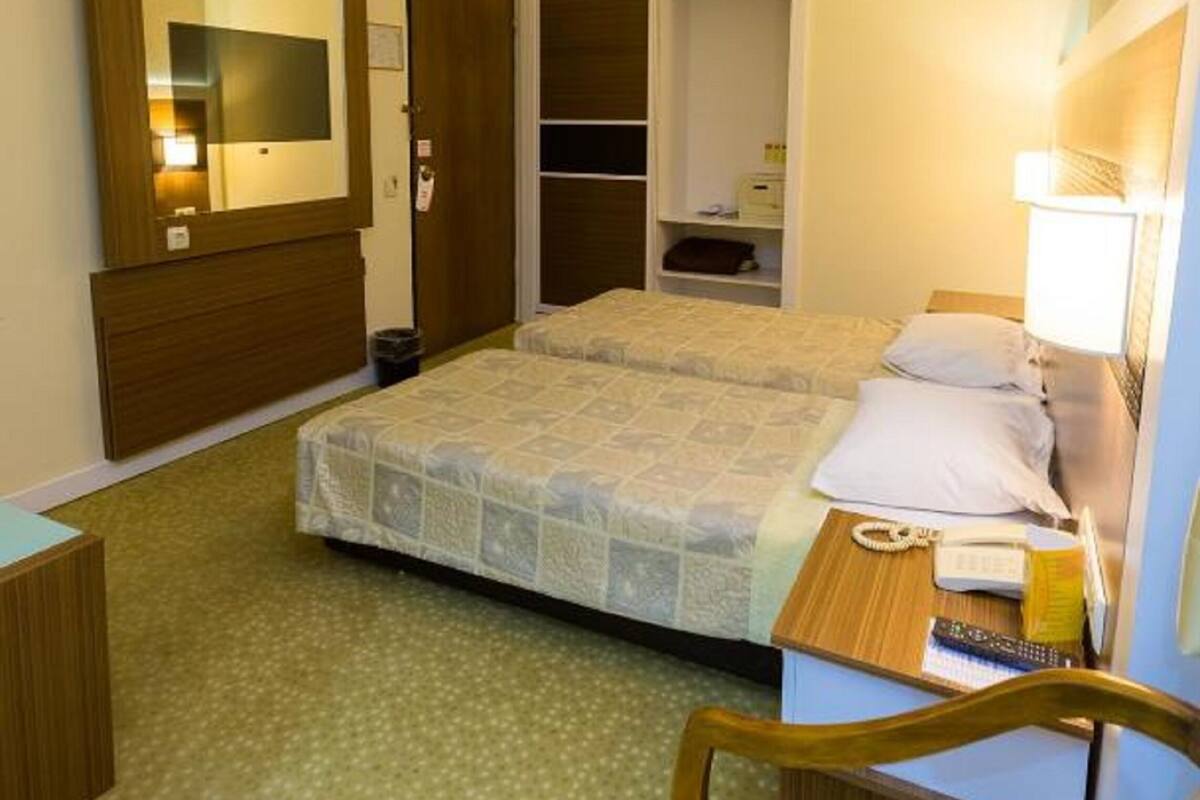 A hotel room with a double bed, a bedside table with a lamp, a chair, a wardrobe, and a mirror.