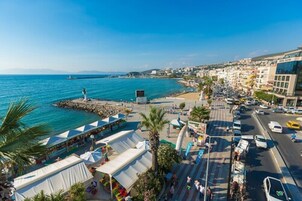 A coastal cityscape with a marina, a statue, and a busy street with cars and pedestrians.