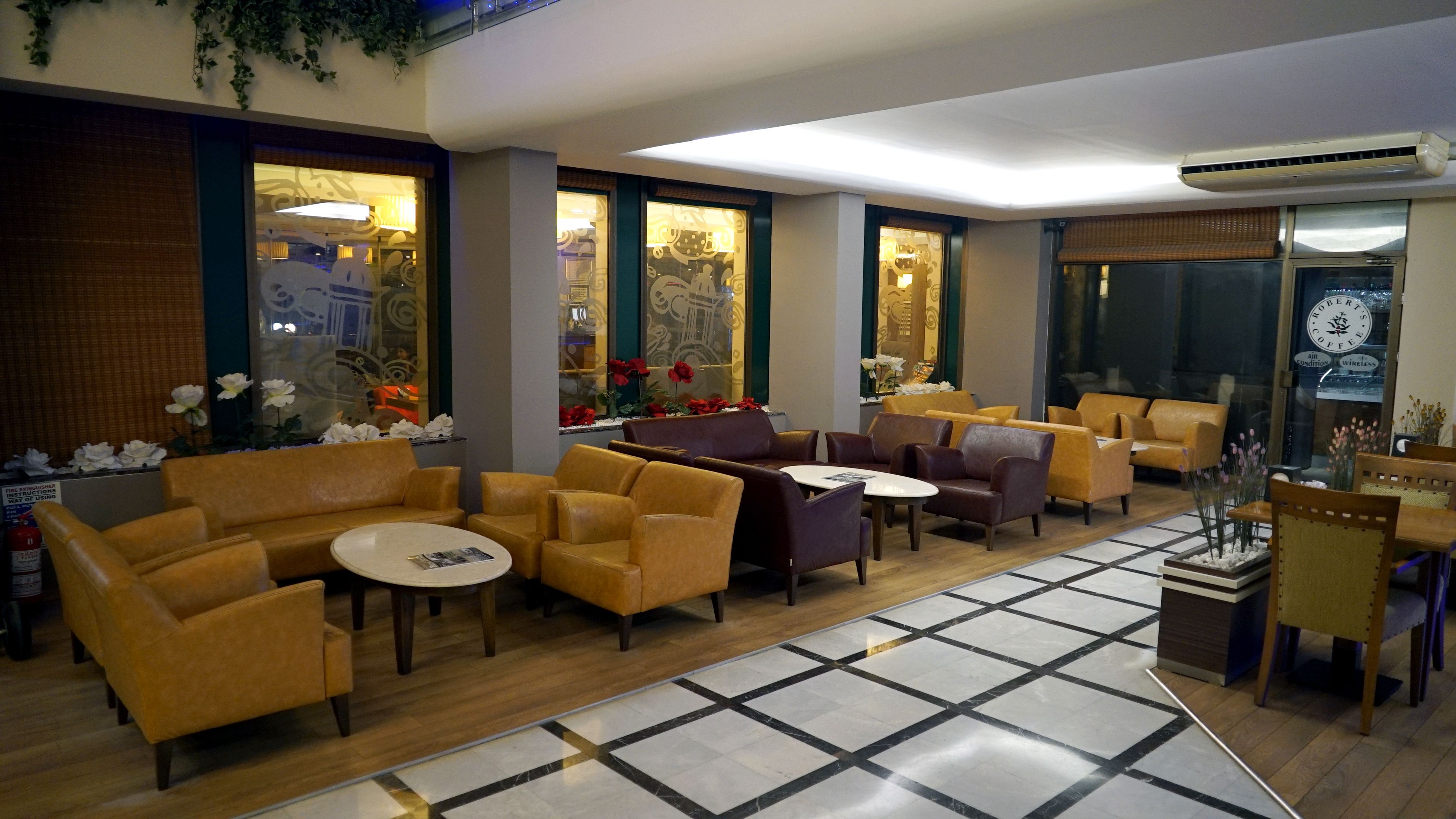 Un vestíbulo de hotel con sofás de cuero, mesas redondas y piso de baldosas.