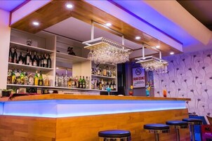 Zona de bar con estantes llenos de botellas, una barra y taburetes.