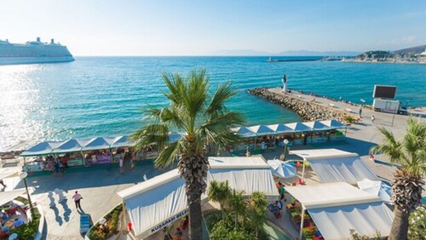 A coastal area with a pier, tents, and a cruise ship in the background. - Derici Hotel (Kusadasi)
