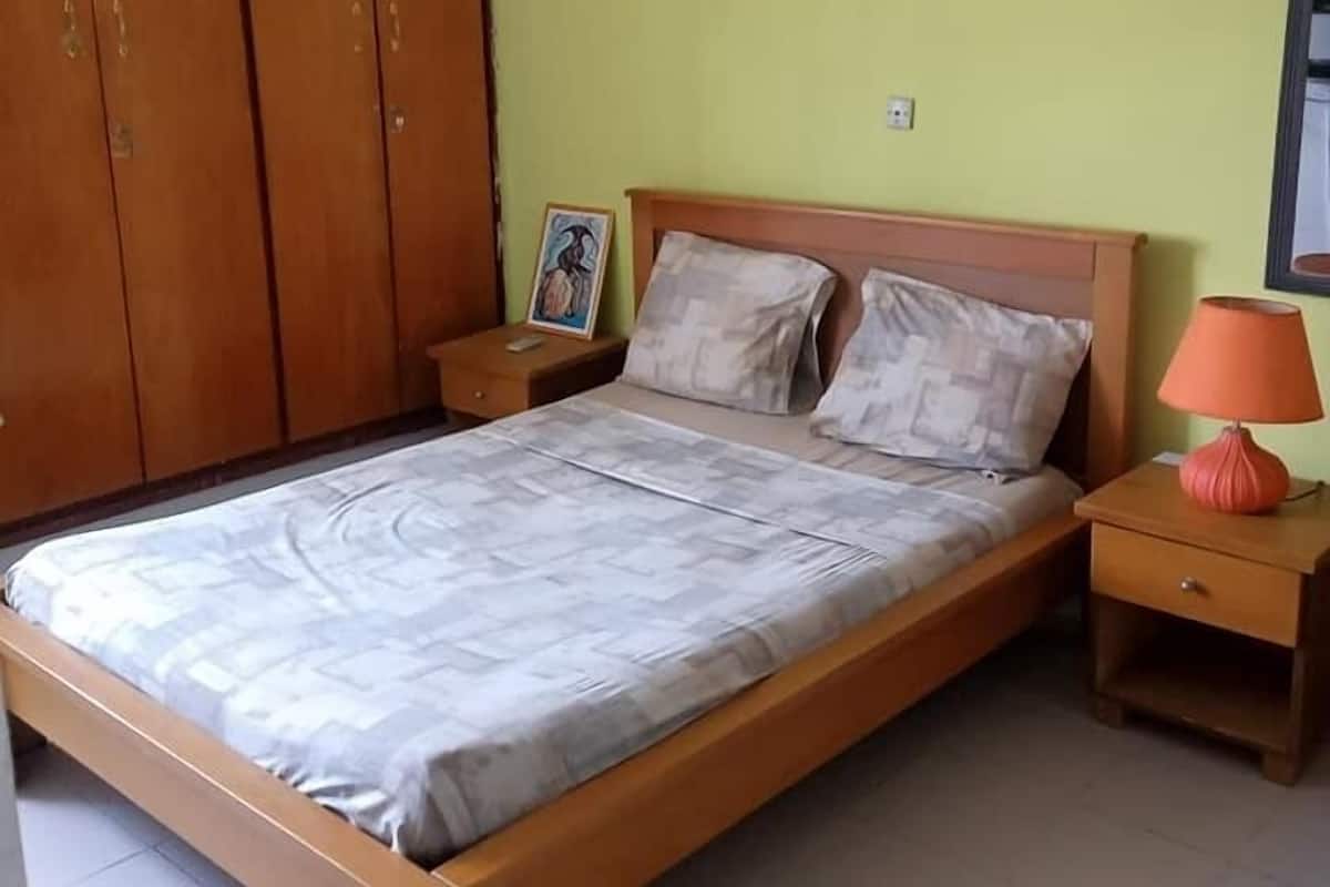 Un dormitorio con cama, armario de madera, mesita de noche con lámpara y aire acondicionado en la pared.