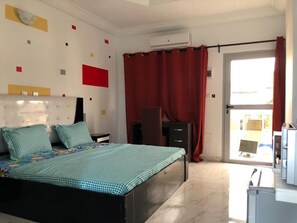 Un dormitorio con cama, cómoda, escritorio y ventana con cortinas rojas.