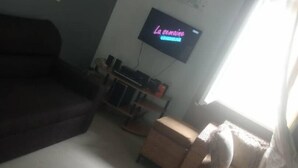 Un salon avec un canapé de couleur sombre, une petite table basse et un téléviseur à écran plat fixé au mur.