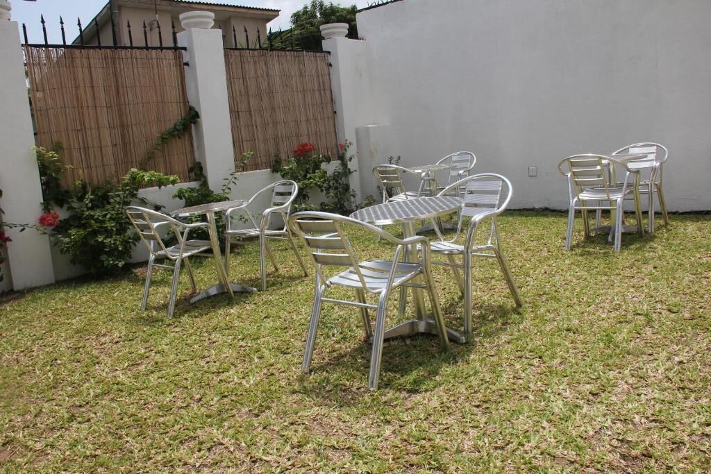 Une terrasse avec des chaises et une table en métal, entourée d’un mur blanc et d’une clôture en bambou.
