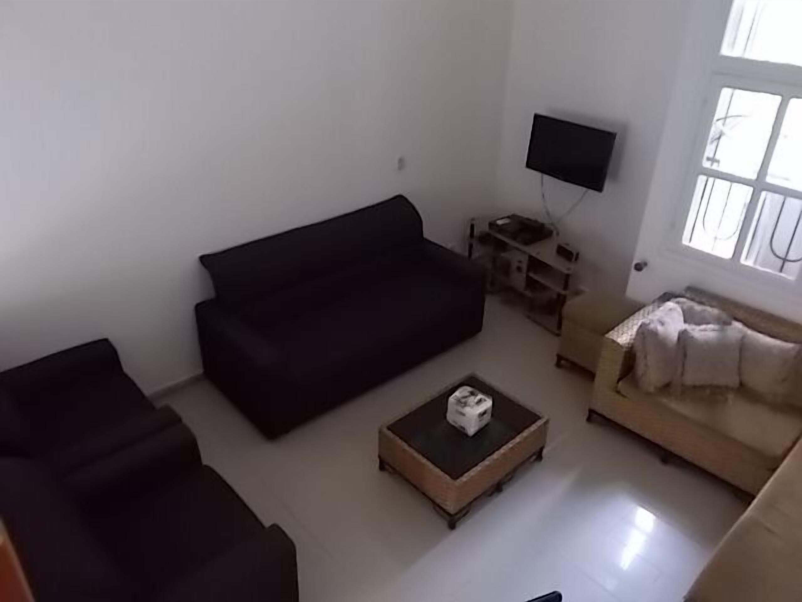 A living room with a dark sofa, a smaller armchair, a coffee table with a box, and a TV on a stand.