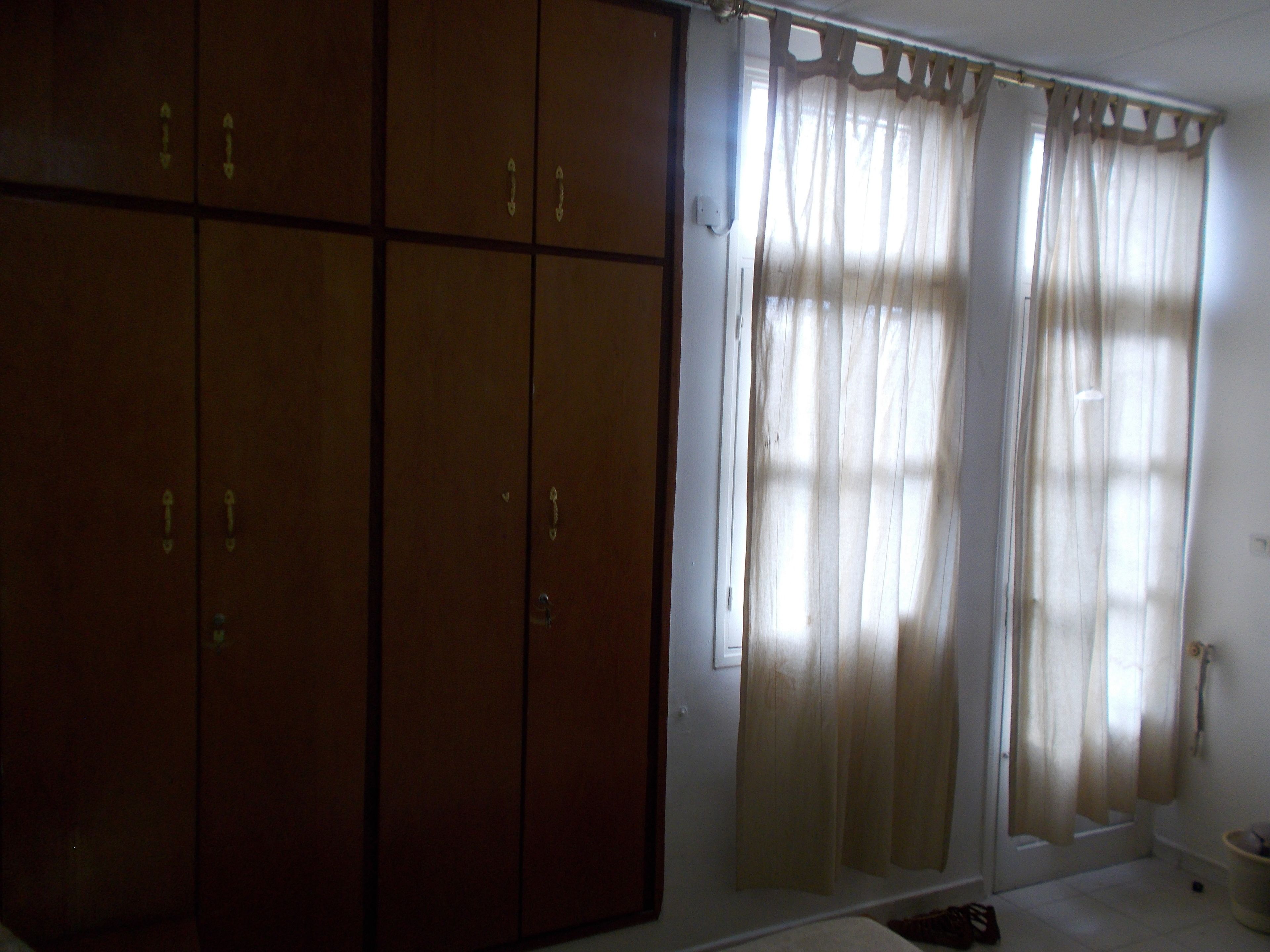 A room with a large wardrobe, a window with sheer curtains, and a white floor.