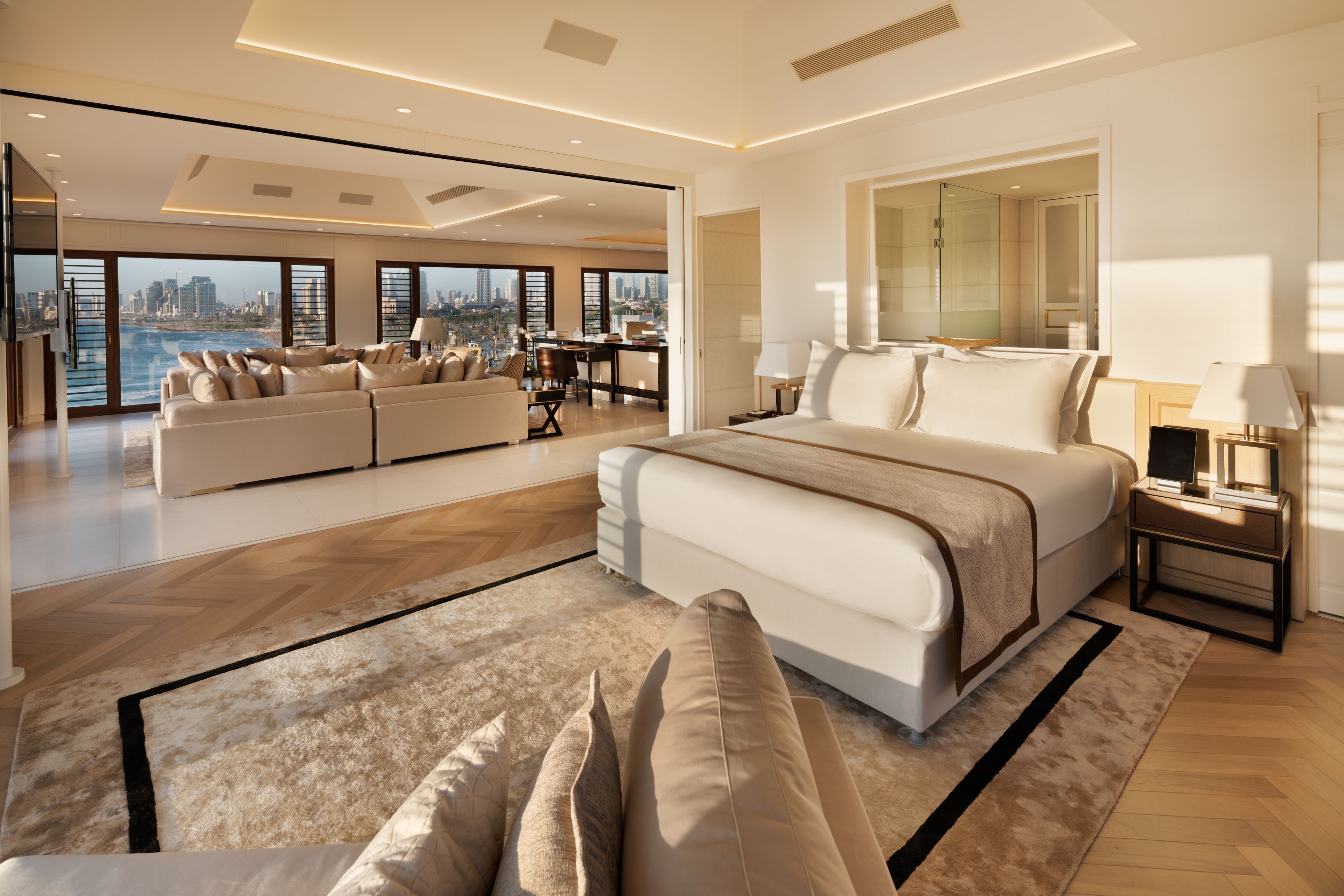 A modern bedroom with a large bed, a sofa set, and a city view.