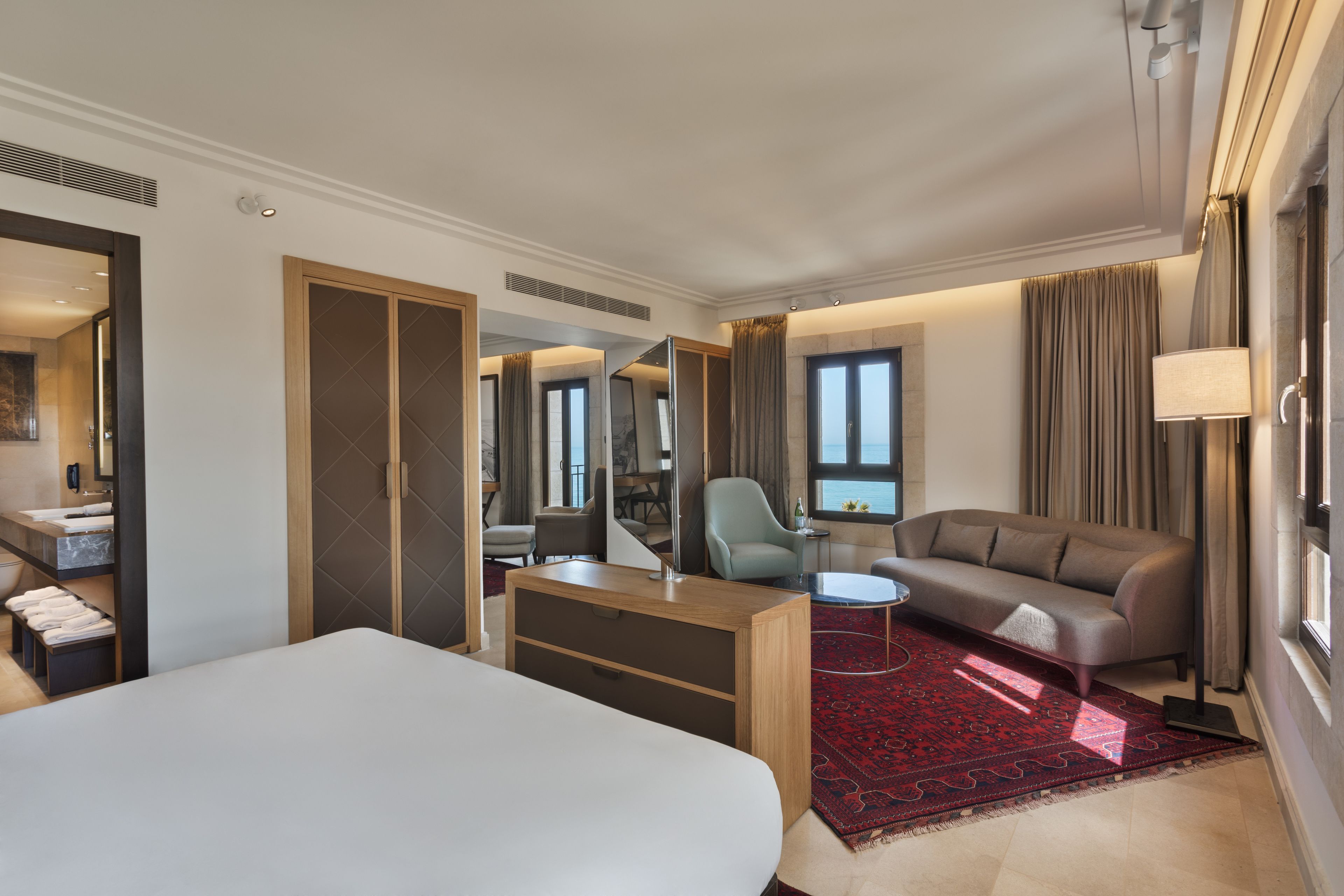 A hotel room with a bed, a sofa, a desk, a chair, and a large window.