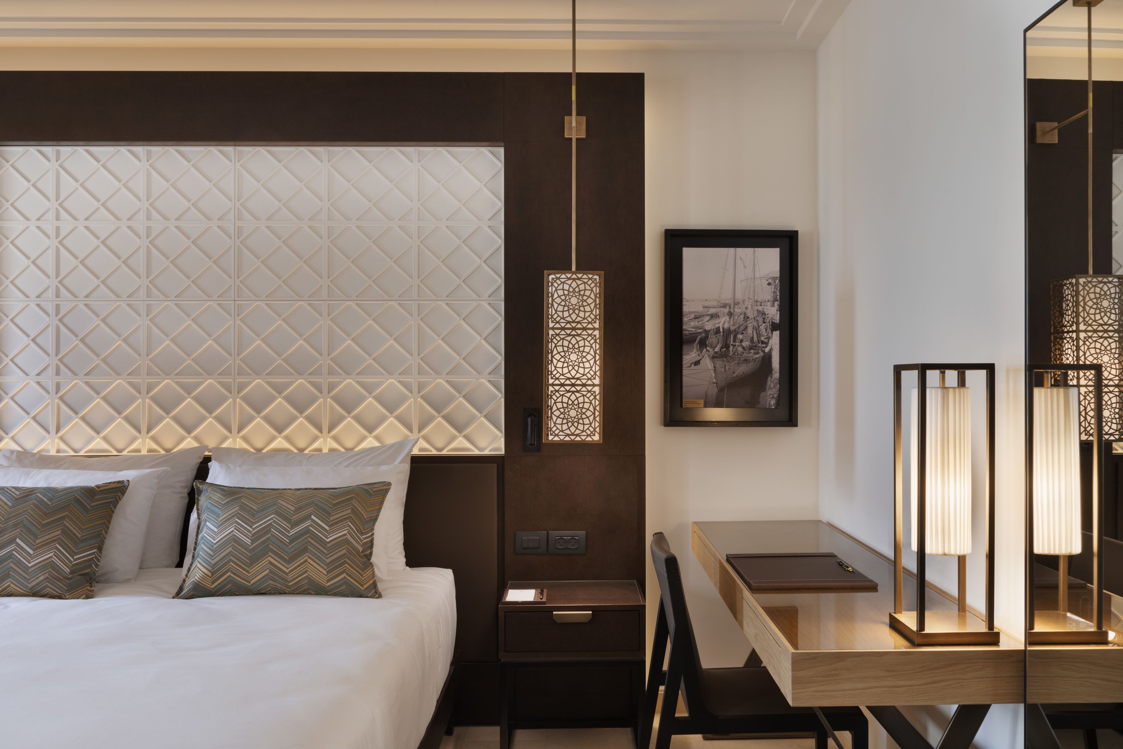Ein modernes Hotelzimmer mit einem ordentlich bezogenen Bett, einem Schreibtisch mit Stuhl und einem großen Spiegel.