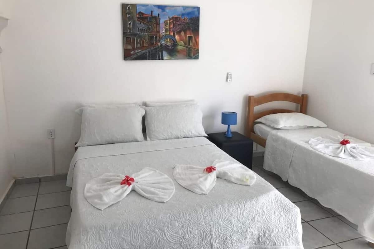 Une chambre d’hôtel avec un grand lit, deux petits lits et un tableau au mur.